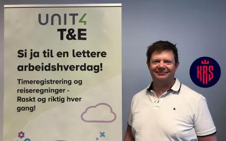 Smilende mann ved siden av en rollup med tekst og Unit4 T&E logo